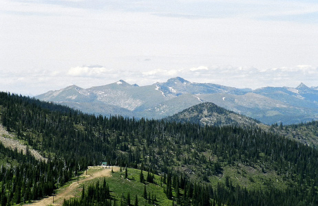 [A scenic view with close mountain peaks in clear view and ones further in the distance with some bits of scattered snow on them a bit greyed.]